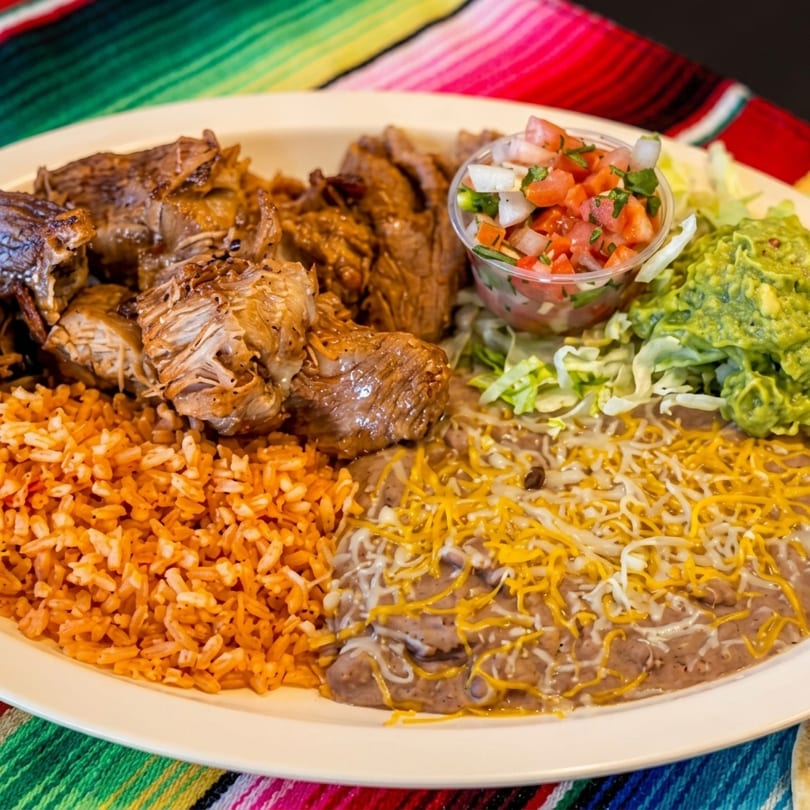 Platter of carnitas, rice, refried beans with cheese, guacamole, pico de gallo, and lettuce.